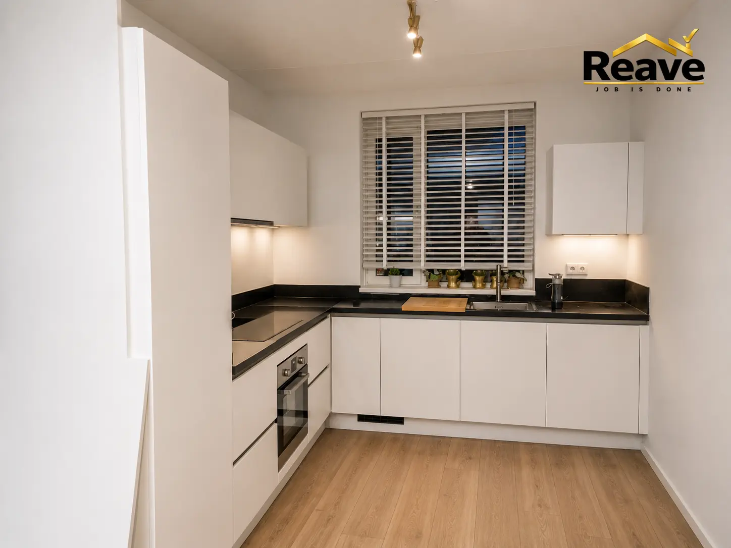 White U-shaped kitchen with black worktop and window blinds