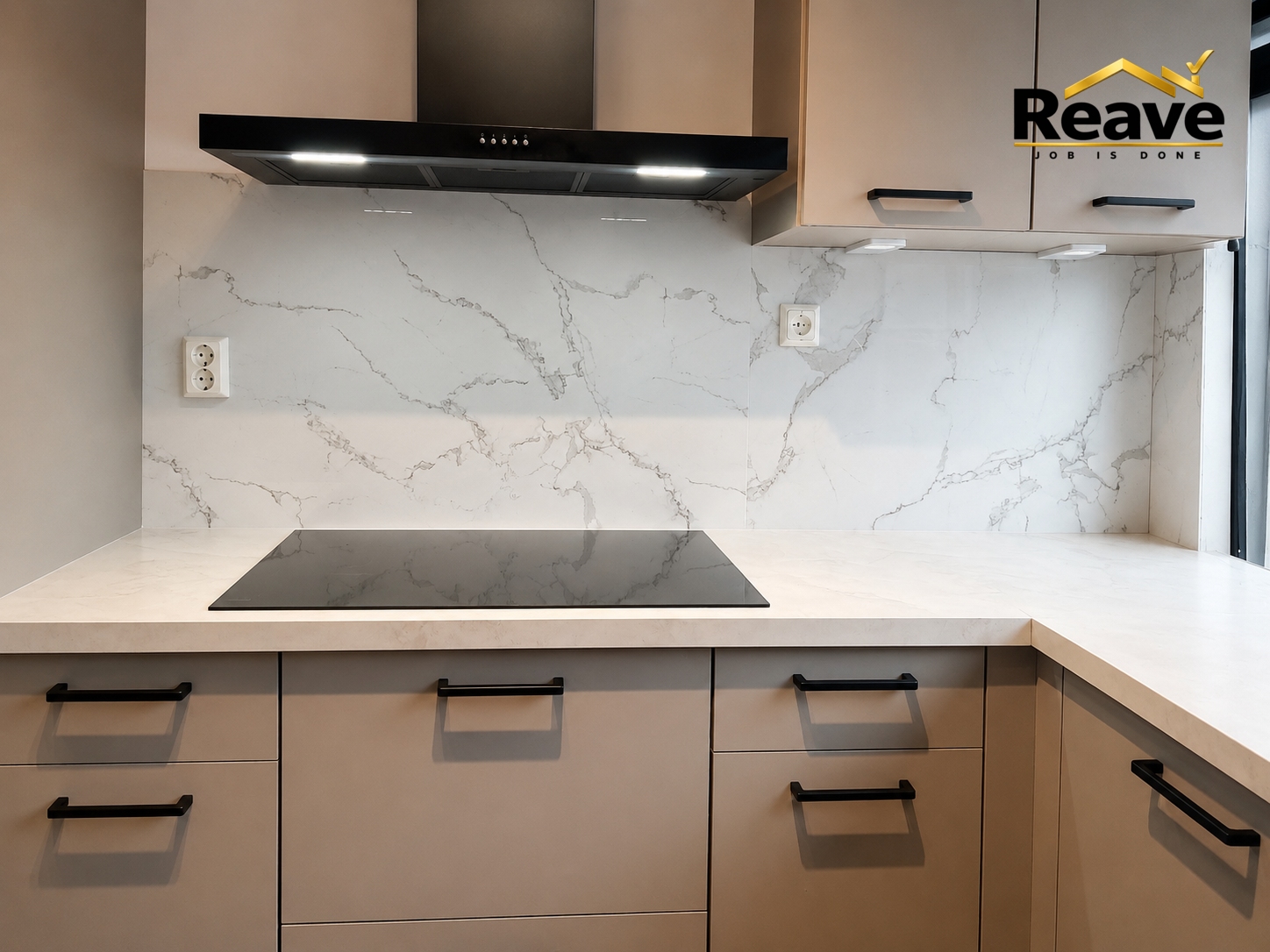Beige handleless kitchen with marble splashback, black extractor and induction hob
