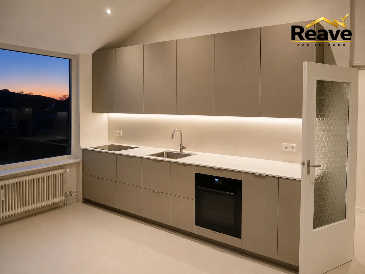 Taupe handleless kitchen under a sloped ceiling at dusk